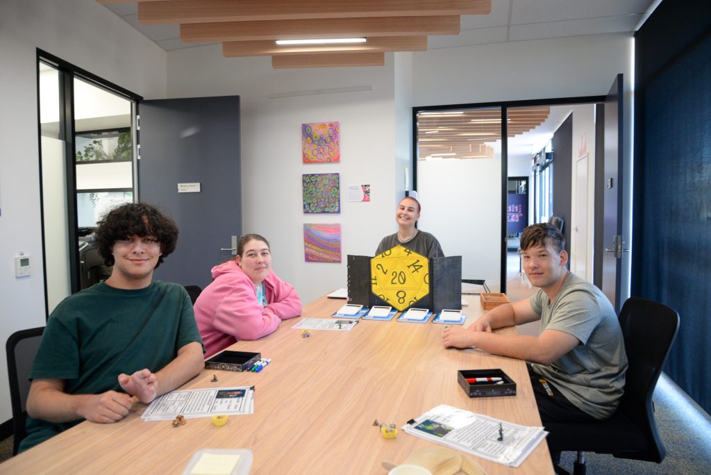 Rocky Bay support worker and customers smiling at the camera while playing a D&D game.