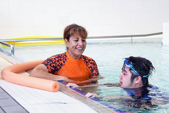 Rocky Bay Senior Allied Health Assistant Sam and Customer Steven are smiling at each other. They are sitting in a pool during Steven's Hydrotherapy session.